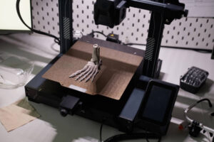 Human foot bone model on aluminum print bed of 3D printer on dim light desk with engineering equipment in laboratory